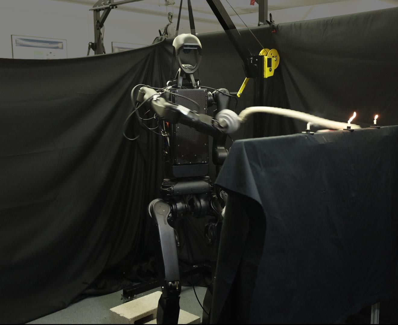 Unitree H1-2 humanoid whipping a rope toward a row of lit candles